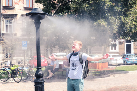Krakow, Poland, July 28, 2018, A young guy is standing under a street water sprayer with arms outstretched and enjoying the coolness escaping from the abnormal heatのeditorial素材
