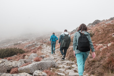 Three tourists people  hike on the stone path in mountain among red grass