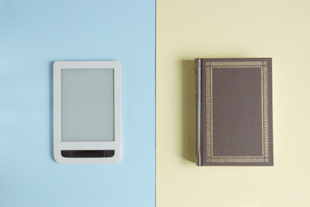 E-book and paper books on blue and yellow pastel backgrounds, concept of confrontation between the old and the newの写真素材