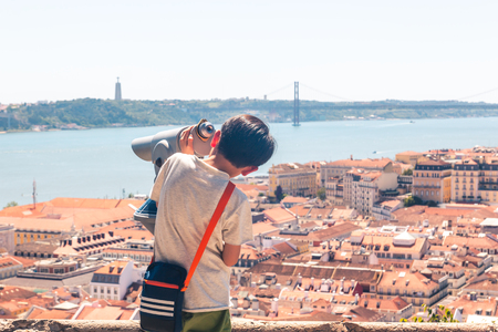 Little boy playing with a binoscope on the observation deck overlooking the old townの写真素材