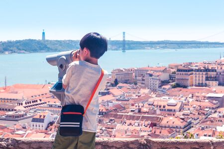 Little boy playing with a binoscope on the observation deck overlooking the old townの写真素材