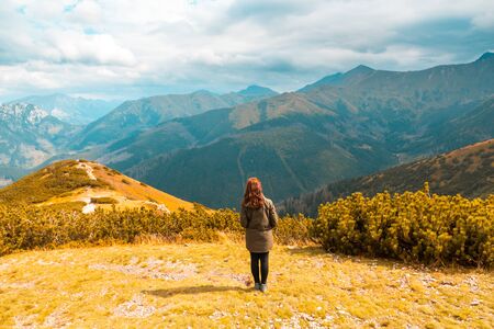 A red-haired girl stands against the background of a stunning autumn mountain landscapeの写真素材