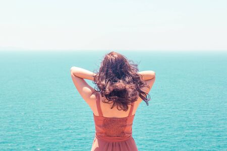 Young girl in dress looking at turquoise seascape and enjoying summer vacationの写真素材