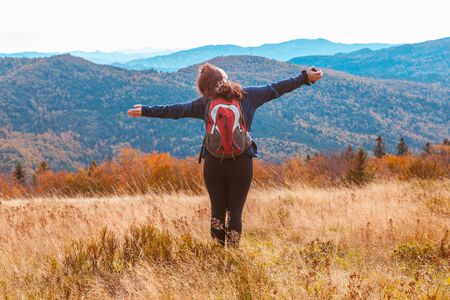 A young girl with her arms spread and her head raised enjoys the autumn warmth and mountain...