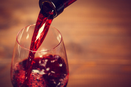 Pouring red wine into the glass against wooden backgroundの写真素材