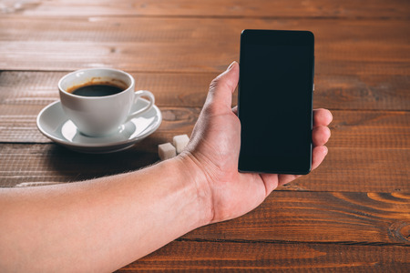 man hand holding a phone with isolated screen  on the wooden background with cup of coffeeの写真素材