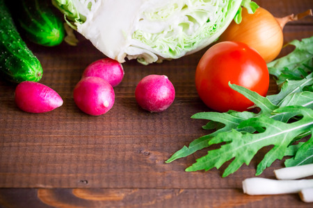 background with old brown boards with fresh healthy vegetables, green onion, radish, cucumber, arugula and cabbage. Empty space for text.の写真素材