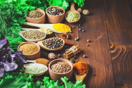 Beautiful colorful spices in wooden spoons and bowls with lettuce, dill and Basil on an old wooden brown table. Free space for your textの写真素材