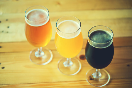 Beautiful background of the Oktoberfest. Glasses of cold fresh white, light and dark beer on the wooden bar counter in the pub. Assorted alcohol in a Flight Ready for Tastingの写真素材