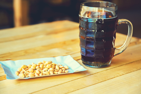 A glass of cold fresh of dark beer and salty peanut on the wooden bar counter in pub with free space for your text. Beautiful background of the Oktoberfest.の写真素材