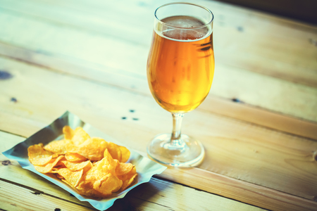 A fresh glass of cold light beer and potato chips on the wooden bar counter in pub with free space for your text. Beautiful background of the Oktoberfest.の写真素材