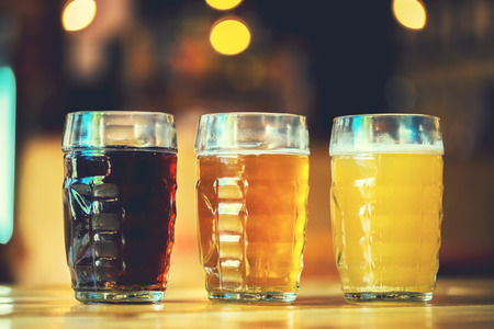 Beautiful background of the Oktoberfest. Glasses of cold fresh white, light and dark beer on the wooden bar counter in the pub. Assorted alcohol in a Flight Ready for Tastingの写真素材