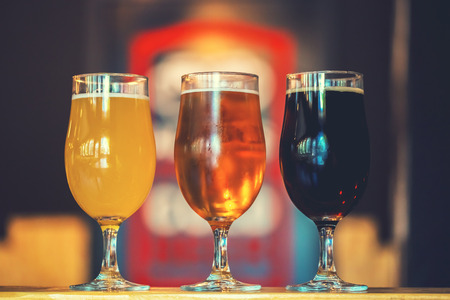 Beautiful background of the Oktoberfest. Glasses of cold fresh white, light and dark beer on the wooden bar counter in the pub. Assorted alcohol in a Flight Ready for Tastingの写真素材