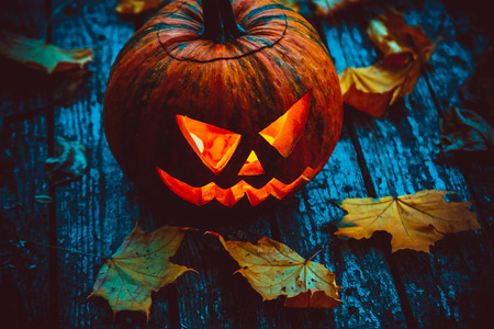 Glowing pumpkin symbolizing the head of old Jack, with autumn leaves on wooden background. Soft focus. shallow DOFの写真素材