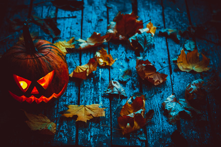 Glowing pumpkin symbolizing the head of old Jack, with autumn leaves on wooden background. Soft focus. shallow DOFの写真素材
