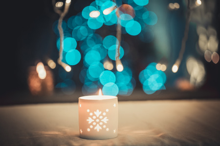 Close-up of Christmas burning candle in a candlestick on blurred background living room with Christmas tree.の写真素材