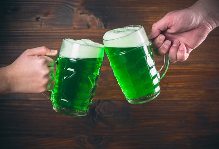 St Patrick's Day concept two mug on hands green beer against wooden backgroundの写真素材