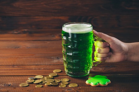 Beautiful background for St. Patrick's day with a female hand holding a glass of green beer, gold...