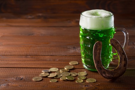 Beautiful background for St. Patrick's day with a glass of green beer, gold coins and a horseshoe on a wooden table. Free spaceの写真素材