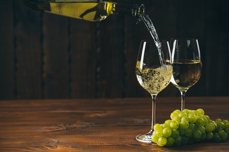 Beautiful white wine in wine glass with a bunch of green grapes against wooden background with free spaceの写真素材