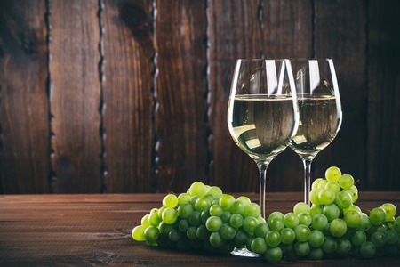 Beautiful White wine in wine glass with a bunch of green grapes, on a wooden background with free...