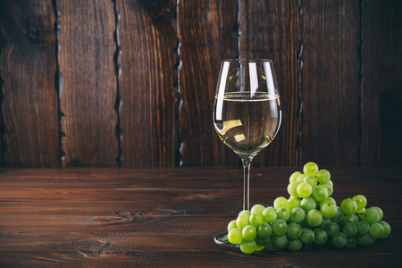 Beautiful White wine in wine glass with a bunch of green grapes, on a wooden background with free spaceの写真素材