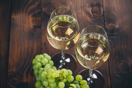 Beautiful White wine in wine glass with a bunch of green grapes, on a wooden background with free spaceの写真素材