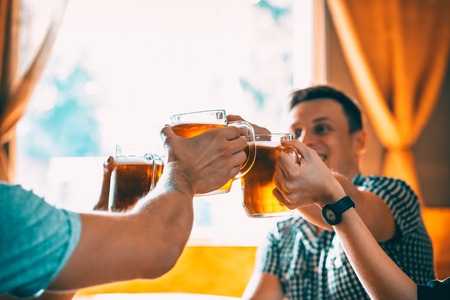 Friends toasting with glasses of light beer at the pub. Beautiful background of the Oktoberfest. A group of young people while relaxing at the bar. fine grain. Soft focus. Shallow DOFの写真素材
