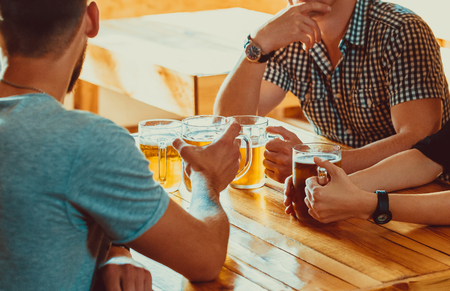 Friends toasting with glasses of light beer at the pub. Beautiful background of the Oktoberfest. A group of young people while relaxing at the bar. fine grain. Soft focus. Shallow DOFの写真素材
