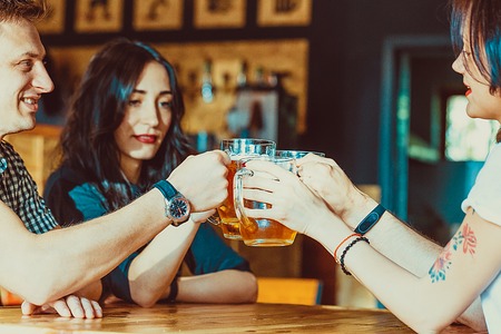 Friends toasting with glasses of light beer at the pub. Beautiful background of the Oktoberfest. A group of young people while relaxing at the bar. fine grain. Soft focus. Shallow DOFの写真素材