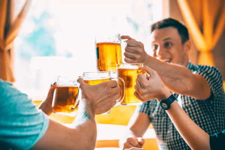 Friends toasting with glasses of light beer at the pub. Beautiful background of the Oktoberfest. A group of young people while relaxing at the bar. fine grain. Soft focus. Shallow DOFの写真素材