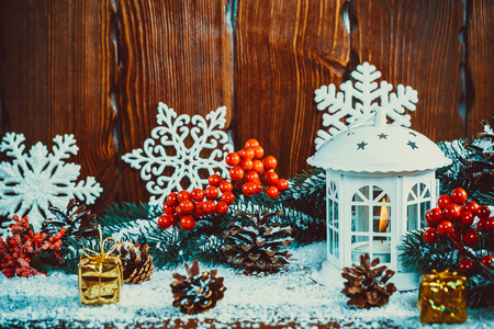 Christmas lantern with lit by candles, Christmas tree branches, gift, cones, snowflakes and snow on vintage wooden background. Free spaceの写真素材