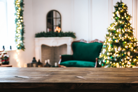 Christmas holiday background with empty rustic table and the bokeh of the living room with the Christmas tree, sofa and fireplace on the second planの写真素材