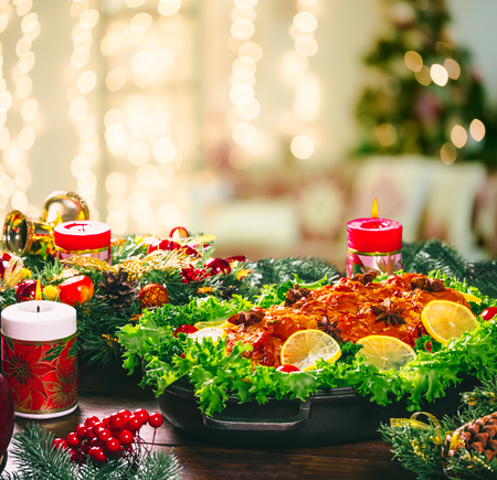 Christmas table dinner time with roasted meats decorated in New Year style on bokeh background the Christmas living room with Christmas tree and fireplace. Thanksgiving day. Beautiful Family holiday.の写真素材