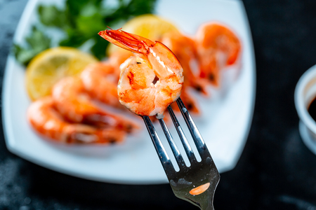 Grilled prawns on fork, behind soy sauce, lemon and herbs. Royal delicious and beautiful peeled shrimp. Flatley. Food background on black stoneの写真素材