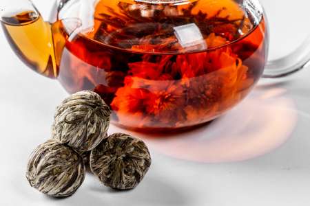 Tea in a glass teapot with a blooming large flower. Teapot with exotic green tea on a white background with dried balls-buds for tea brewingの写真素材