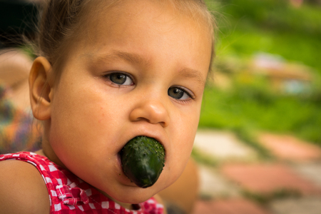 a little girl with a cucumber in her mouth. Children.の写真素材