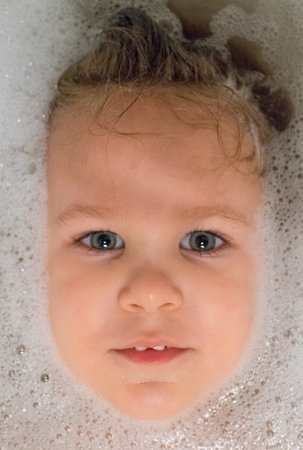 child girl bathes in a bathtub with foam white bath blonde contented face smile beautiful eyes wet...
