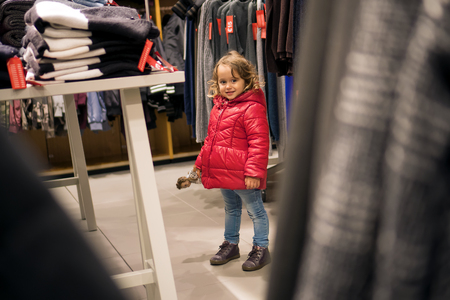 Little Girl in red jacked Looking Curiously in the Store for Salesの写真素材