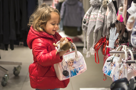 Little Girl in red jacked with a bag Looking Curiously in the Store for Salesの写真素材