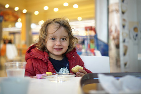happy little girl eating a cake in a mallの写真素材