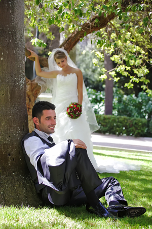 the groom sits on the grass and the bride behind him out of focusの写真素材