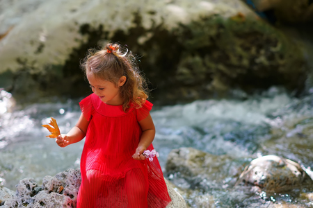 Little girl in red dress sits by the river in Evia, Greeceの写真素材