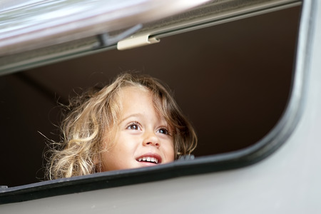 the little girl looks out happy of the camper windowの写真素材