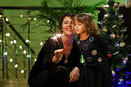 Mom and daughter play with bright stars near the Christmas tree