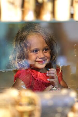 Beautiful little girl looks in the window of a shop in OIA, and makes many funny faces