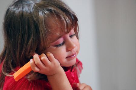 A three year old girl plays with a carrot and squints her eyes