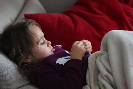 A three year old girl relaxes on the sofa at home