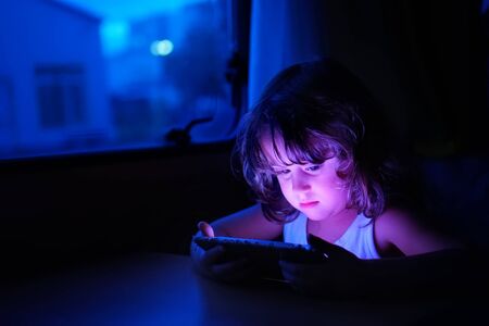 Little girl with cellular and blue evening lightの写真素材