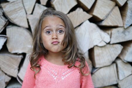 Portrait of 4 year old girl on background of chopped wood that makes funny faceの写真素材